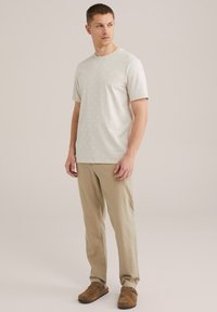 Világos bézs, rövid ujjú póló, finom textúrával, világos khaki nadrággal és barna velúr, slip-on cipővel párosítva.