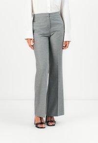 Pantalons gris taille haute avec une coupe droite, fabriqués en tissu texturé. Associés avec des sandales à talons hauts noires. Couture latérale et poches visibles.
