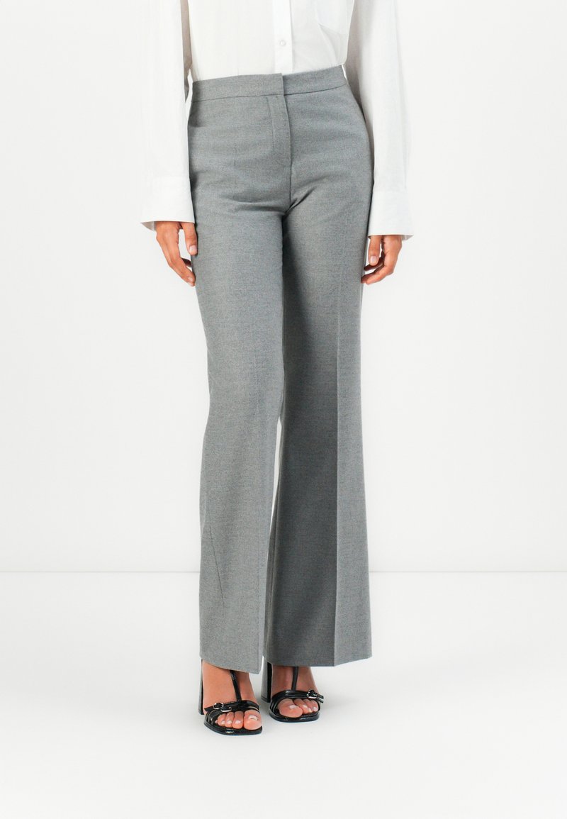 Pantalons gris taille haute avec une coupe droite, fabriqués en tissu texturé. Associés avec des sandales à talons hauts noires. Couture latérale et poches visibles.