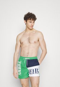 Pantaloni da bagno con un pannello verde con la scritta "TOMMY", una sezione blu navy e un pannello bianco con la scritta "JEANS"; materiale leggero e ad asciugatura rapida.