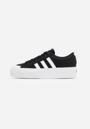 Sort lavsnøresneaker med hvid platformsål, hvid tåhætte, sorte snørebånd og tre hvide striber på siden.
