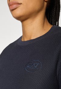 Tengerészkék környakú pulóver, texturált anyaggal, bordázott gallérral és kontrasztos kék színű hímzett EA7 logóval.