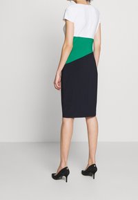 Färgblockad klänning med en figurnära silhuett; vit överdel, grön mittpanel och marinblå botten. Mjukt tyg, knälång, korta ärmar.