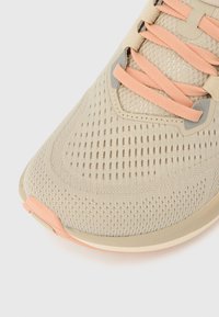 Tuvplāns ar bēša krāsas elpojošas acs sporta apaviem ar persiku krāsas šņorēm un teksturētu zoles detaļu.