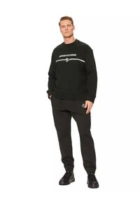 Sudadera negra con el logo "Armani Exchange" en blanco, combinado con pantalones de chándal negros. Diseñado en un corte relajado, presenta puños acanalados y un acento decorativo.