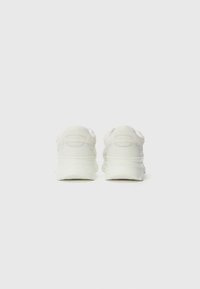 Hvite sneakers med teksturert overdel, polstret krage og kraftig såle. Bakfra viser de en jevn overflate og lette detaljer på hælen.