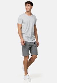 Grijze v-hals t-shirt en grijze shorts, gemaakt van een stof met een gladde textuur. De shorts hebben een zichtbare zijzak en een merklabel. Witte sneakers.