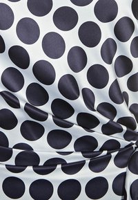 Tissu en satin avec un fond clair comportant de grands pois bleus marine. La texture semble lisse avec un léger éclat. Réduit les plis et les froissements.