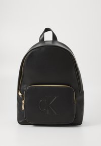 Rucsac din piele neagră cu o formă rotunjită, fermoar auriu și un buzunar frontal cu un logo "ck" aplicat. Textură netedă pe toată suprafața.