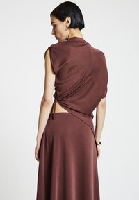 Robe drapée bordeaux à manches courtes, avec un détail noué à la taille et un dos ouvert. Fabriquée en tissu doux et extensible.
