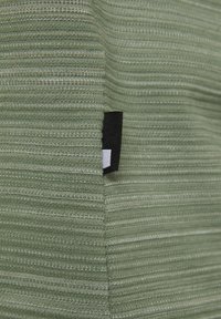 Grüner, gerippter Stoff mit strukturierter Oberfläche, der an der Kante ein kleines schwarz-weißes Etikett zeigt. Nahaufnahme des Materials.