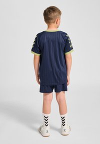 Ungdomsidrottsutrustning med marinblå randig tröja, kontrasterande limegrön krage, matchande shorts och mönstrade strumpor med svart chevrondesign.