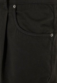 Pantalons en denim noir avec une poche avant, un bouton-pression argenté et des coutures contrastées. Le tissu semble robuste avec une texture lisse.