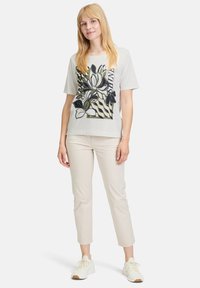T-shirt blanc à manches courtes avec un motif floral en noir et vert. Assorti à un pantalon beige clair ajusté et des baskets blanches.