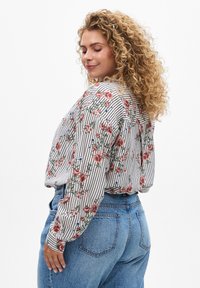 Long-sleeved blouse featuring bold red roses and blue flowers on a white striped background. Made of lightweight fabric with a relaxed fit.