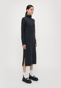 Strikket turtleneck-kjole i mørkegrå, med lange ermer og sidespalter, kombinert med kraftige svarte platåsko og hvite sokker.