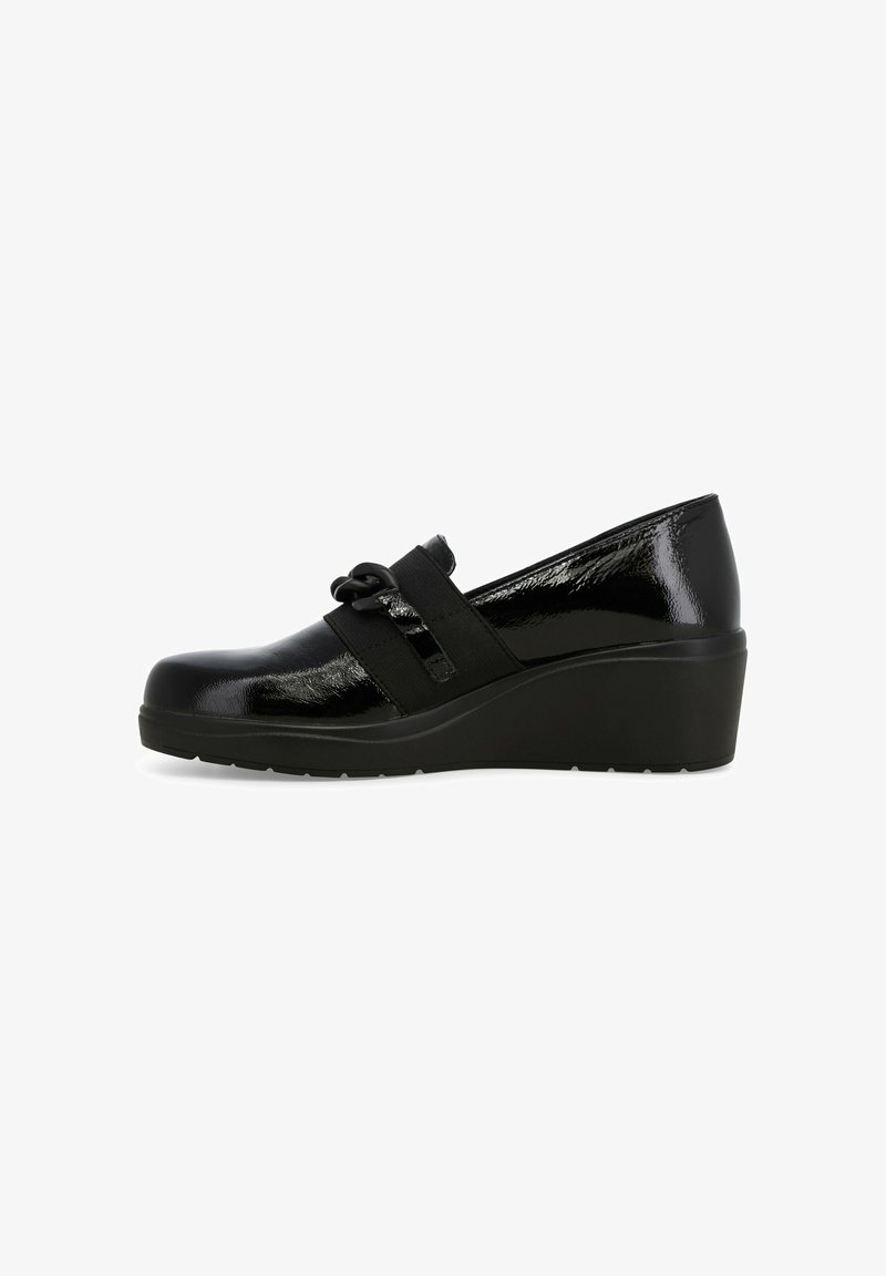 Mocassino con tacco a zeppa lucido nero, dotato di una fascia elastica e di un dettaglio decorativo a catena nera sul lato, mostrato in profilo su sfondo bianco.