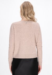 Beige kötött pulóver puha textúrával, hosszú ujjal és kerek nyakkivágással. A hátsó részen egy kis márkacímke található.