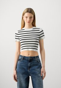 Svart og hvit stripete crop top med korte ermer, laget av ribbestrikket materiale, paret med høytlivede blå denimbukser.