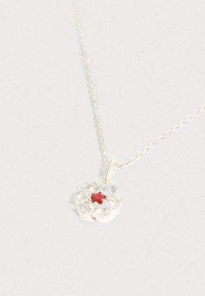 Collier argenté avec un pendentif floral orné d'une pierre rouge centrale et de pierres claires entourantes, présentant une finition polie et une chaîne délicate.
