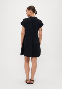 Rochie neagră cu mâneci scurte, confecționată dintr-un material ușor, cu talie ajustată și fustă evazată. Design minimalist, până la genunchi, cu o textură subtilă.