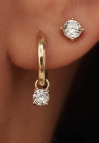 Boucle d'oreille en or avec une pierre précieuse transparente suspendue et un clou en pierre précieuse transparente plus petit. Texture lisse, formes rondes et réglages à griffes sûrs.