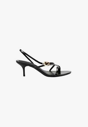 Sandalia negra de tacón con tiras finas, puntera abierta, diseño de tipo slingback y un pequeño óvalo decorativo dorado en la tira superior.