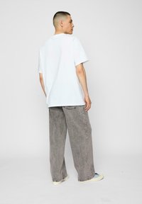 Hvid kortærmet t-shirt parret med løse grå jeans, som har en afslappet pasform og let tekstur, sat mod en ensfarvet baggrund.