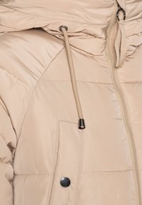 Beige pufferjakke med lynlås, justerbar snørehætte og en knappet lomme. Glat, skinnende tekstur og quiltet design.