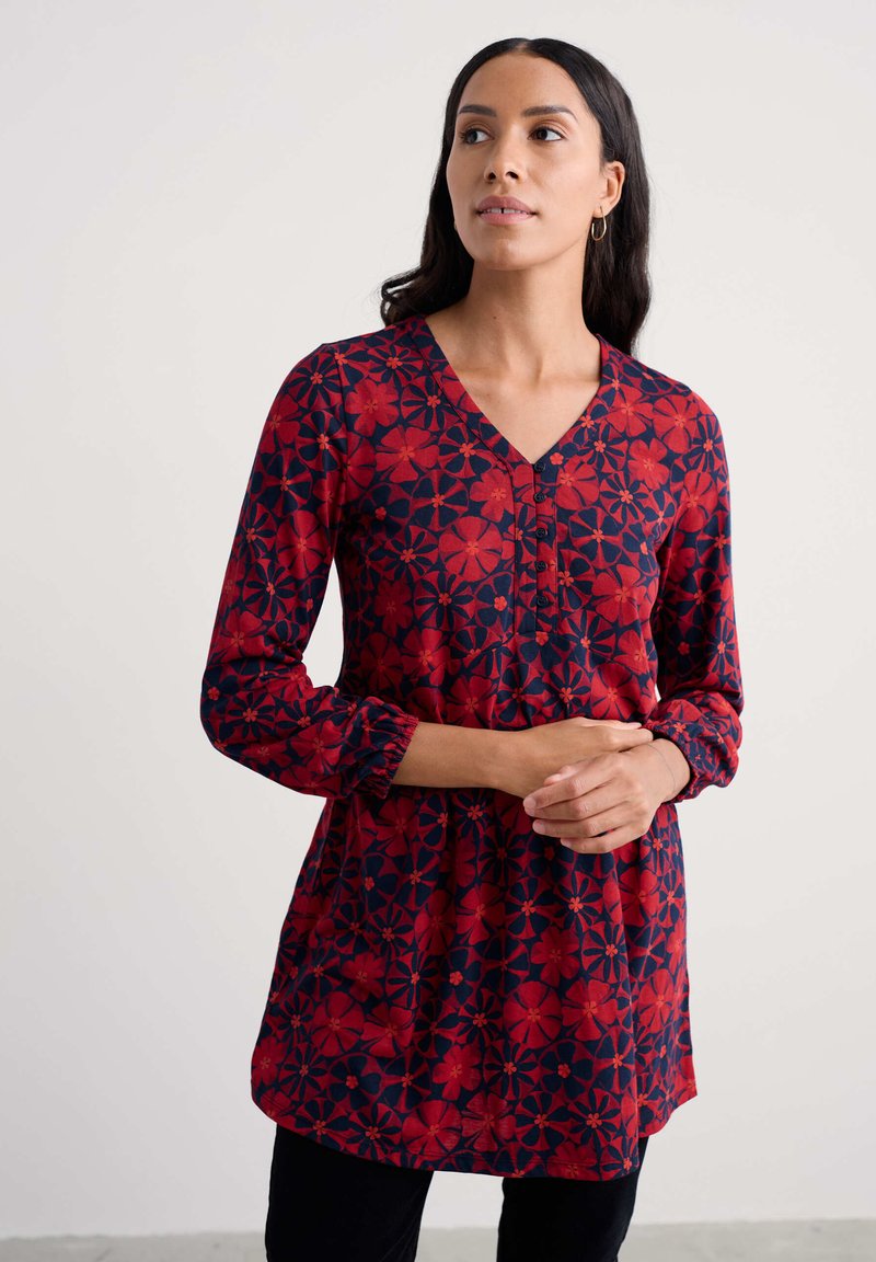 Raudona ir tamsiai mėlyna gėlių tunika su V formos iškirptė, ilgomis rankovėmis, mygtukų priekyje ir surinktomis apykaklėmis, su žaismingu gėlių raštu.