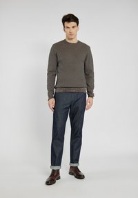 Brązowy sweter w wzory, ciemnot denimowe spodnie i brązowe skórzane botki. Sweter ma teksturowany wzór i ściągacze; dżinsy podwinięte na kostkach.