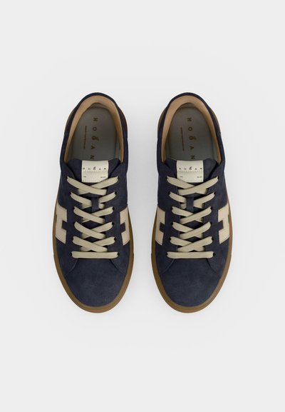 Paire de baskets en daim bleu marine avec lacets beige et bandes latérales beige, vues de dessus sur fond blanc.