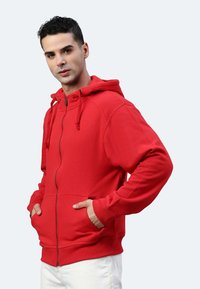 Felpa rossa con zip, cappuccio, tasche a marsupio e polsini elastici. Materiale in cotone liscio, vestibilità casual e colore uniforme senza fantasie.