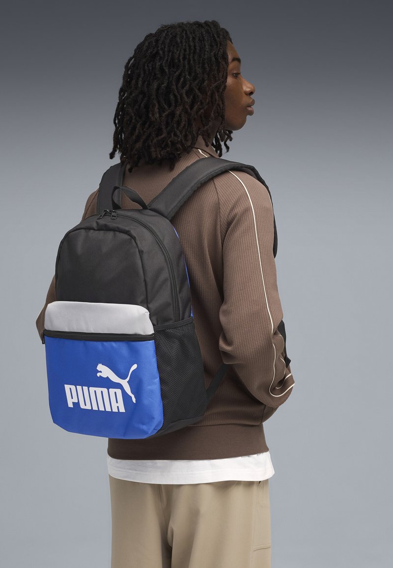 Zaino Puma nero e blu con una parte superiore grigia, caratterizzato da un grande logo bianco sul davanti, spallacci regolabili e tasche in rete.