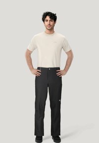 Zwarte wandelbroeken met een minimalistisch ontwerp, gecombineerd met een lichtbeige t-shirt. De broek heeft een knoopsluiting en zijzakken.