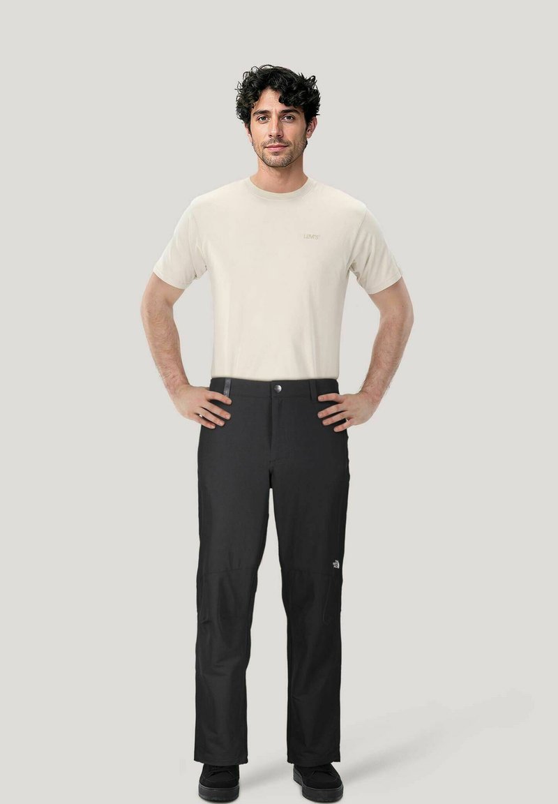 Zwarte wandelbroeken met een minimalistisch ontwerp, gecombineerd met een lichtbeige t-shirt. De broek heeft een knoopsluiting en zijzakken.