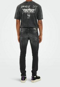T-shirt graphique noir avec impression blanche, associé à un jean en denim foncé et des baskets noires avec des accents violets contrastés et une semelle texturée.