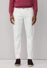 Pantalon en denim blanc avec une coupe droite, affichant un design classique à cinq poches et des ourlets retroussés. Associé à un pull bordeaux et des chaussures foncées.