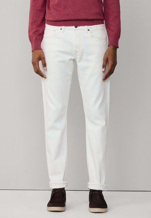Pantalones de mezclilla blancos con un corte recto, que presentan un diseño clásico de cinco bolsillos y puños enrollados. Combinados con un suéter burdeos y zapatos oscuros.
