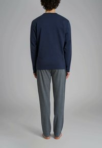 Camicia a maniche lunghe in cotone navy abbinata a pantaloni da pigiama grigi a righe. Tessuto morbido, vestibilità rilassata e cuciture e polsini visibili.