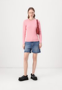 Rosa kabelstrikket genser, dongerishorts og svarte platåklosser. Genseren har rund hals og tettsittende mansjetter, mens vesken er rød.