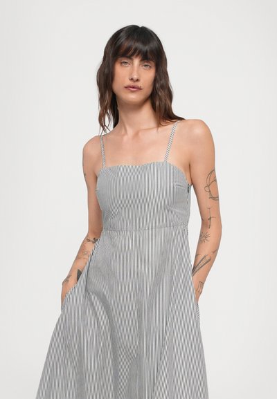 Gestreiftes, ärmelloses Kleid in Schwarz und Weiß, mit einem figurbetonten Oberteil und einem fließenden Rock, seitlichen Taschen und einer glatten Stofftextur.