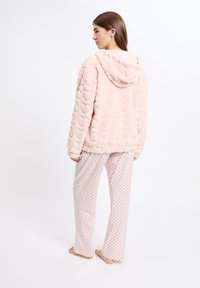 Jasnoróżowa bluza z kapturem z sztucznego futra z motywem serc, zestawiona z białymi spodniami do piżamy w drobne czerwone kropki. Miękka faktura, luźny krój.