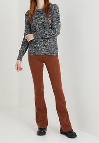 Dunkelgrauer melierter Pullover mit langen Ärmeln, kombiniert mit figurbetonten, rostfarbenen Schlaghosen und schwarzen Stiefeletten.