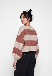 Maglione accorciato a strisce beige e ruggine, texture a maglia, maniche ampie, orlo a coste e scollatura rotonda. Presenta una vestibilità rilassata.