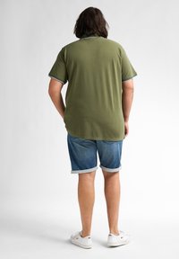 Oliwkowa koszulka polo z krótkim rękawem i białymi wykończeniami; zestawiona z podwiniętymi dżinsowymi szortami i białymi trampkami. Prosty design bez wzorów.