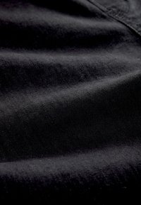 Close-up van zwarte denimstof die textuur en stiksels toont met zachte plooien en schaduwen.