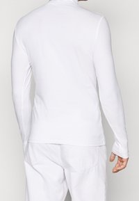 Langärmliges, weißes Rollkragenshirt aus glattem, elastischem Stoff mit taillierter Passform. Verfügt über einen hohen Kragen und nahtlose Schultern.
