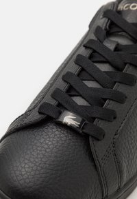 Baskets noires en cuir texturé, dotées de lacets plats noirs, d'une forme élégante et d'un petit logo sur la languette.