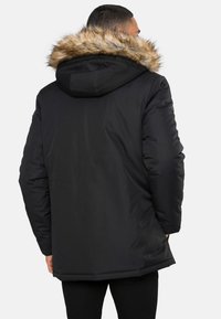 Sort parka-jakke med hætte beklædt med kunstpels, lynlåslommer og længere snit for bedre dækning. Glat stof med isolering.